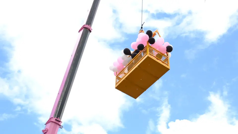 Picture of a man cage covered in pink and white balloons on the day of the Pink Lady crane launch